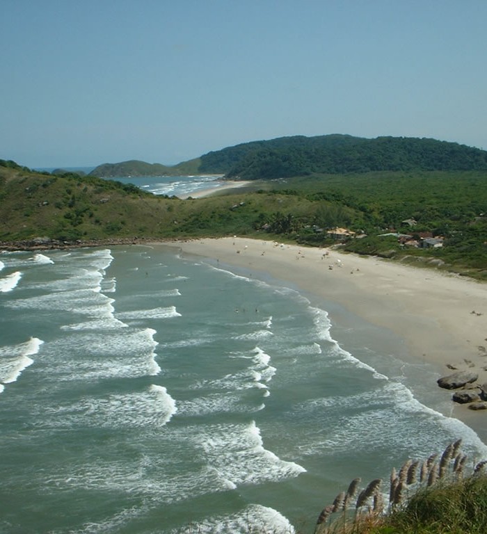 Foto da Praia Grande sobre o morro do Farol, ondas do mar à esquerda e praia com areia à direita